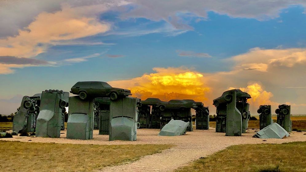 Carhenge, as the sun is setting with a storm in the background.