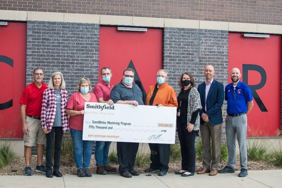 Paul Doremus, plant manager of Smithfield’s Crete facility presents a $50,000 donation on behalf of the company to Zoe White, program coordinator for TeamMates Mentoring Program, members of the TeamMates board and school administration in front of Crete H